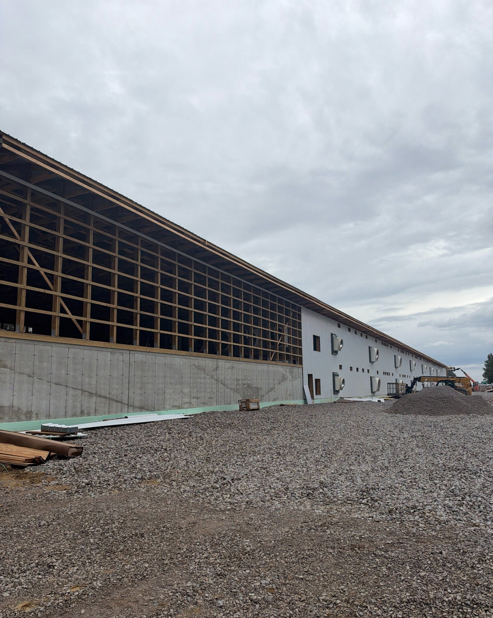 Side of a long wood and steel framed building under construction