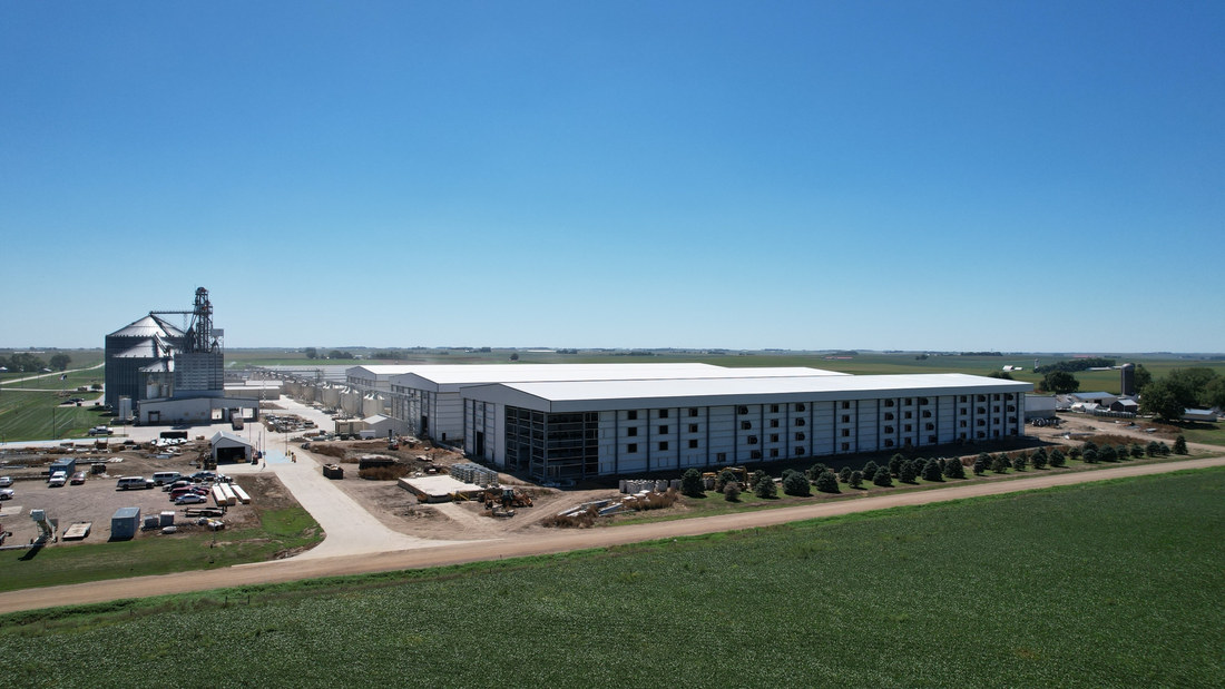 Side view of the long metal layer facility building across a farm field in Iowa