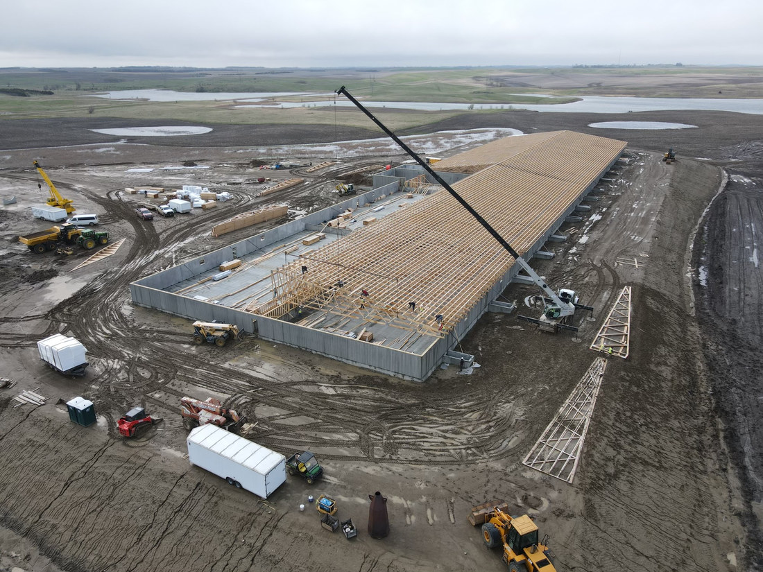 Crane and crew setting roof trusses over concrete walls on a South Dakota ag building